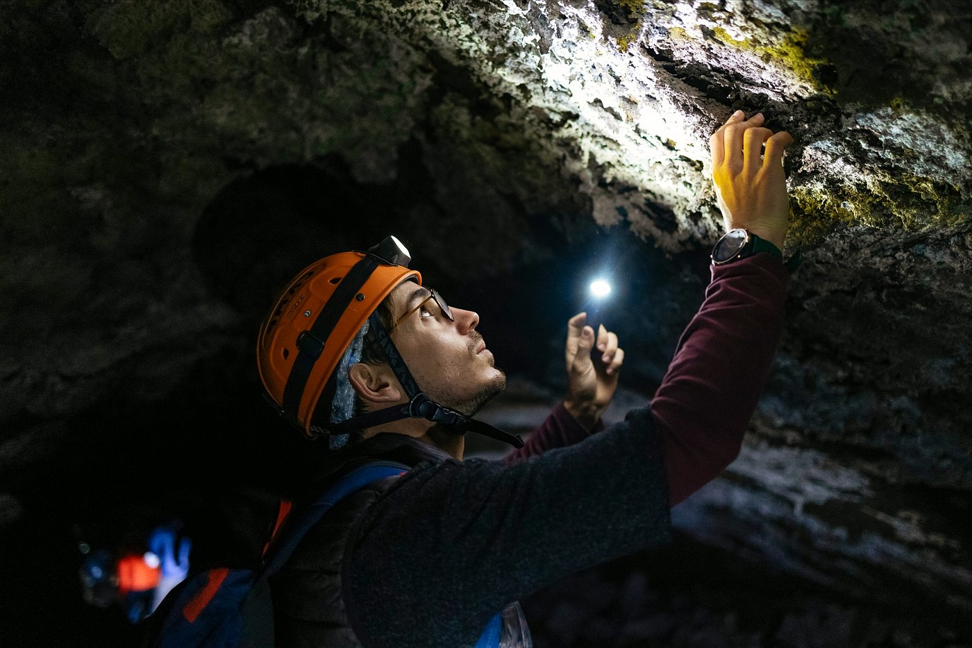 Etna sunset tour guest exploring a lava cave with a head torch